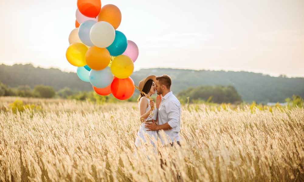 Love couple with balloons hugs in a rye field